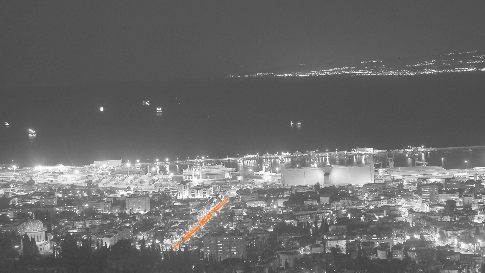Haifa bay at night from Mount Carmel in black and white, one avenue of lights in orange. Photo: David King, CC BY 2.0, via Wikimedia Commons