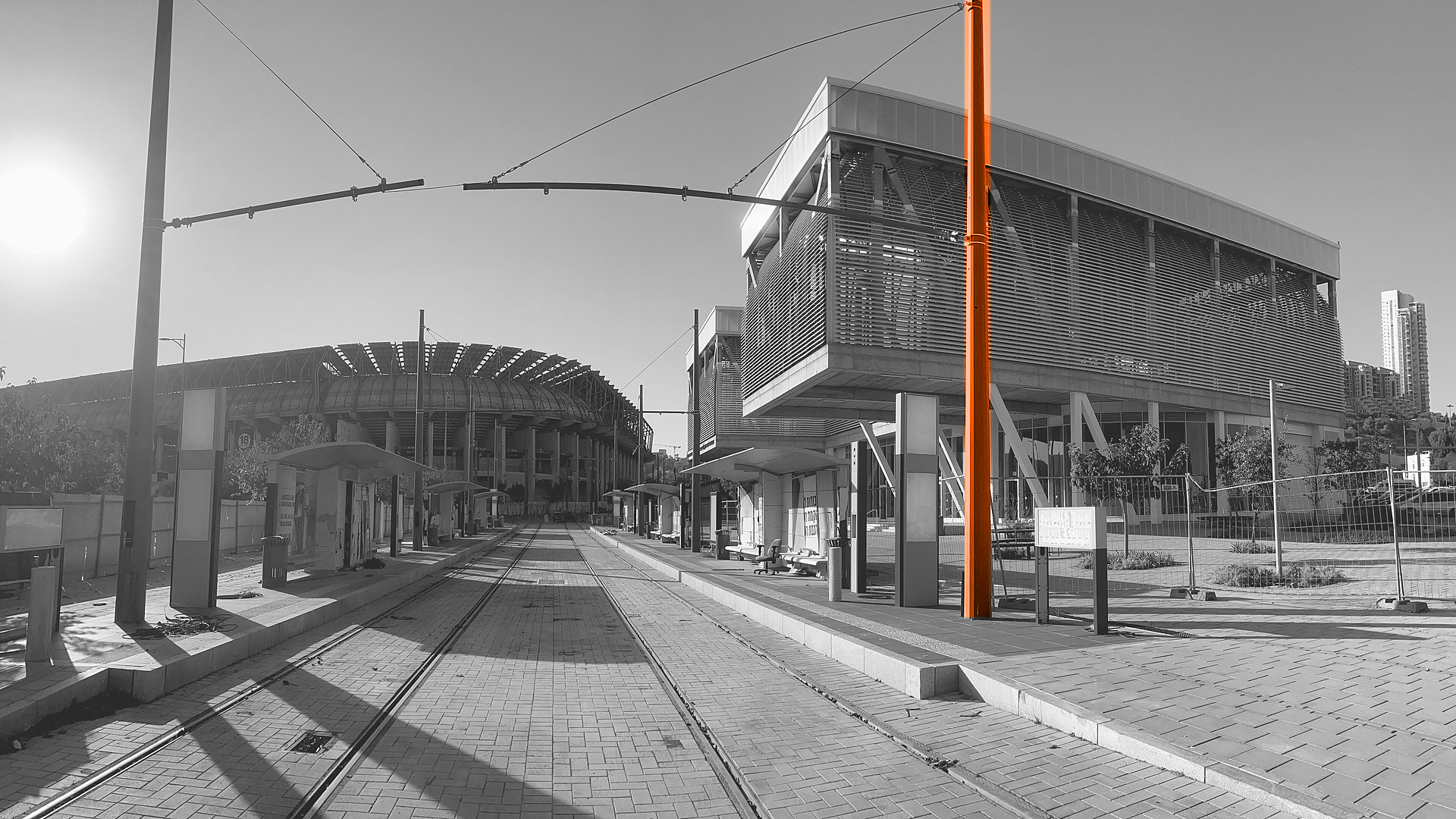 Black-and-white photo of the Sports Complex Malha light-rail station in Jerusalem, with a catenary pole highlighted in orange