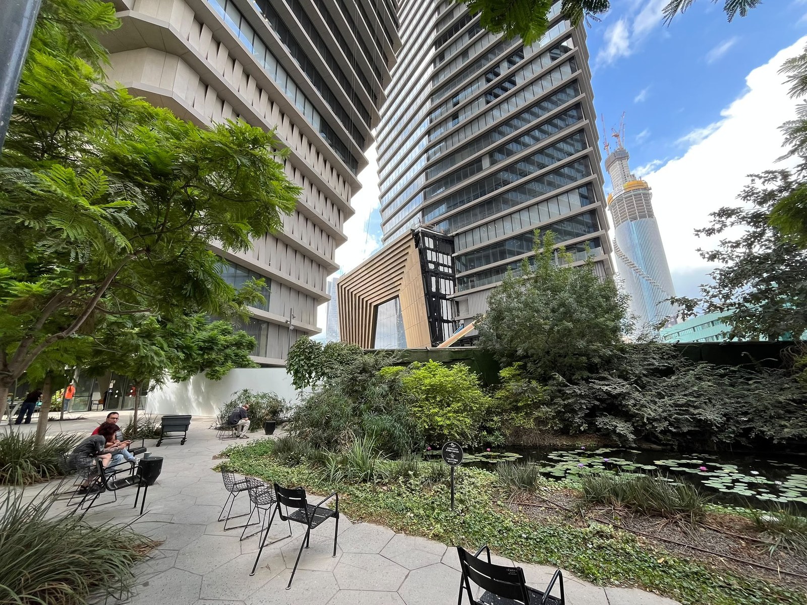 Landscaped plaza with a lily pond, hexagon paving and black chairs at the foot of the EAST&TLV towers