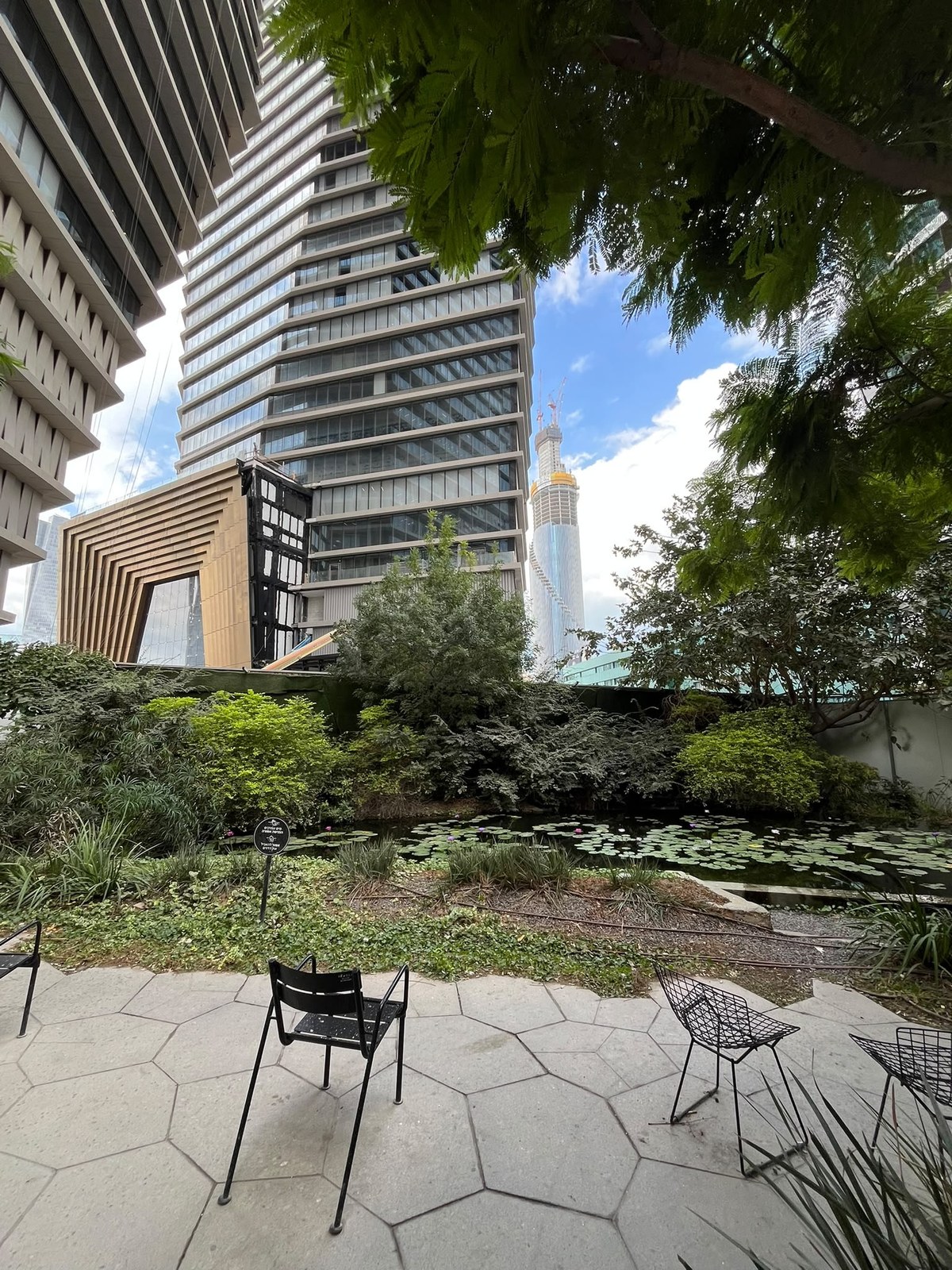 Hexagon-paved patio facing a lily pond, with the bronze-toned entrance and the ToHa tower behind