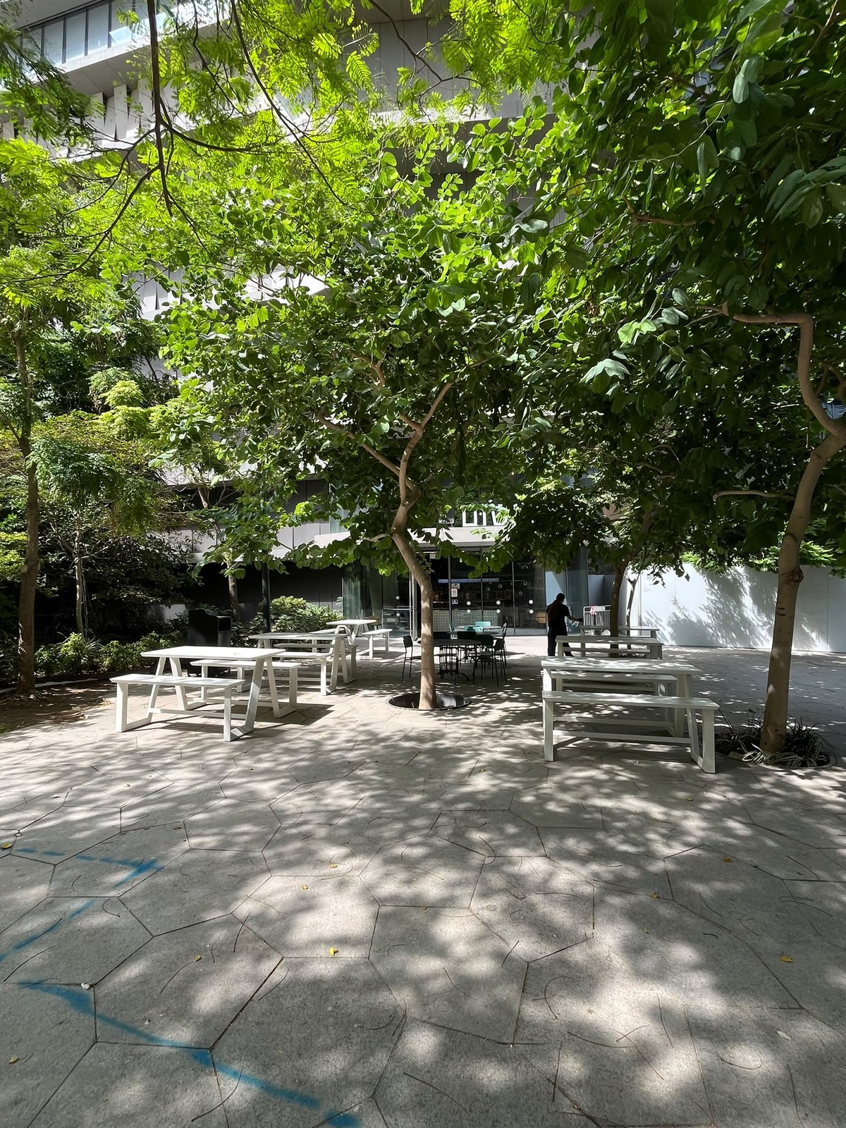 Shaded patio with hexagonal stone paving, white picnic tables and mature trees at the foot of the towers