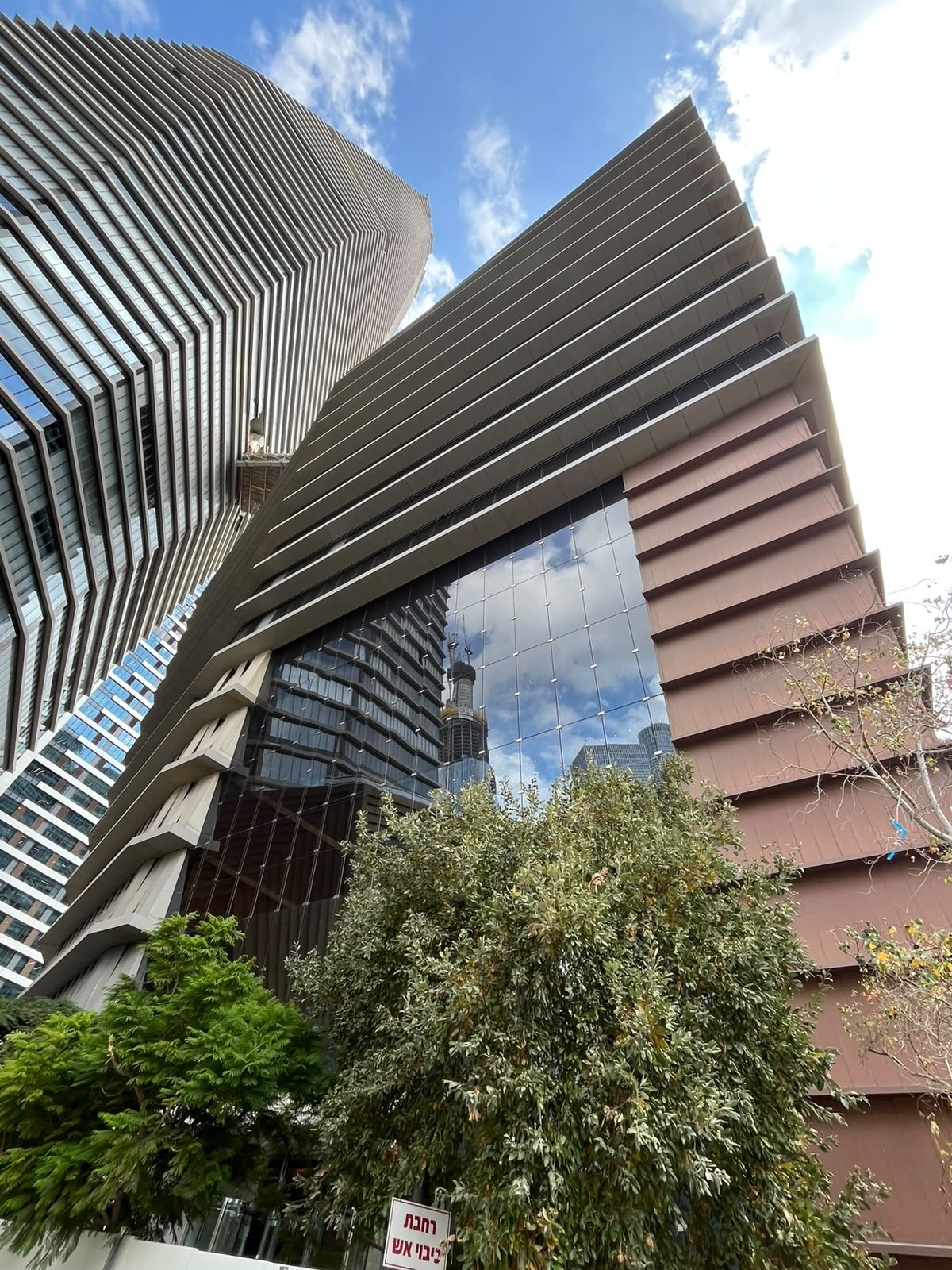 Bronze-toned horizontal slats and a mirrored glass facade rising above the greenery, seen from below